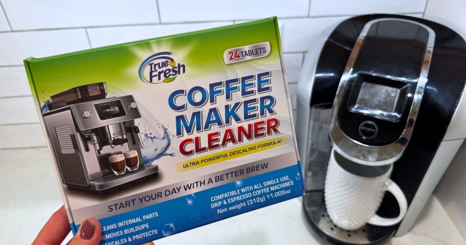 hand holding a box of True Fresh Coffee Machine cleaner tablets next to a coffee machine