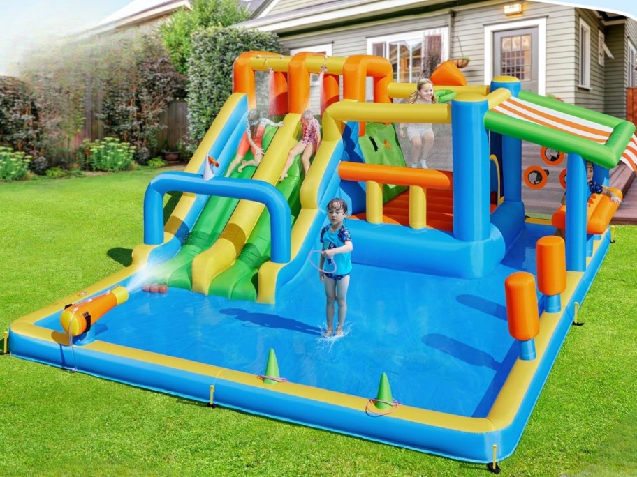 kids playing on a huge inflatable water slide in a backyard