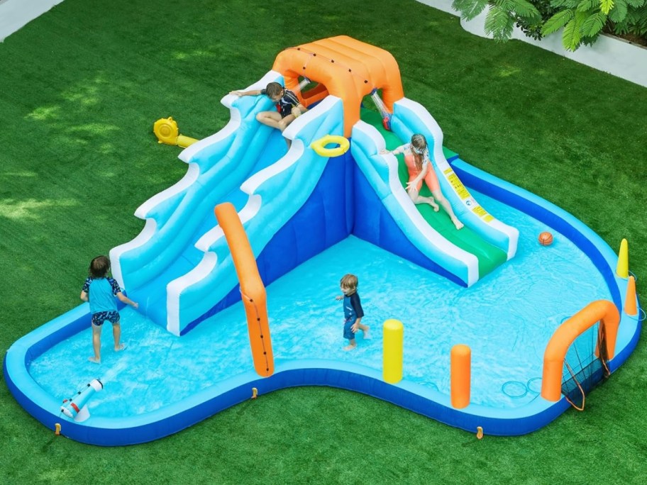 kids playing on a huge inflatable water slide in a backyard