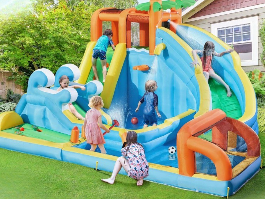kids playing on a huge inflatable water slide in a backyard